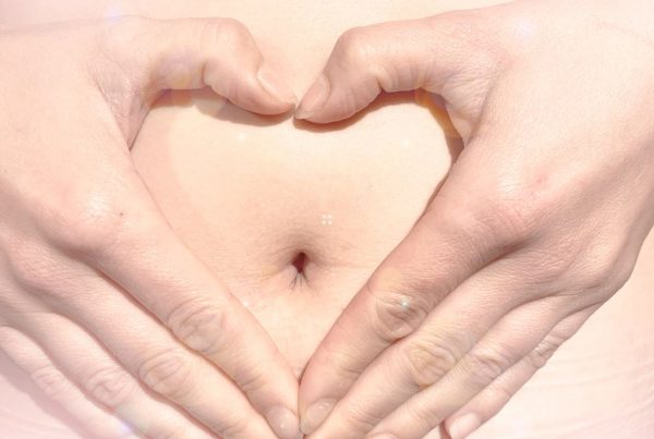 Woman's hands on her belly in the shape of a love heart
