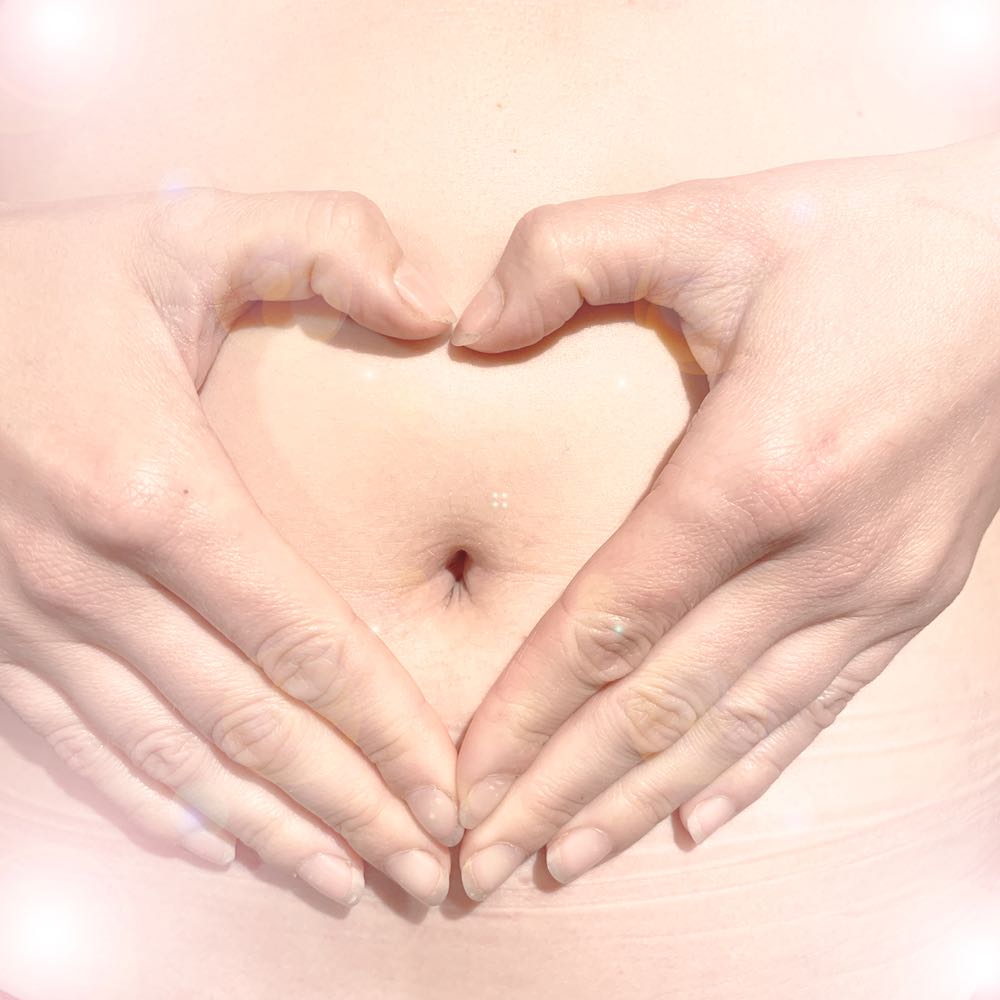Woman's hands on her belly in the shape of a love heart