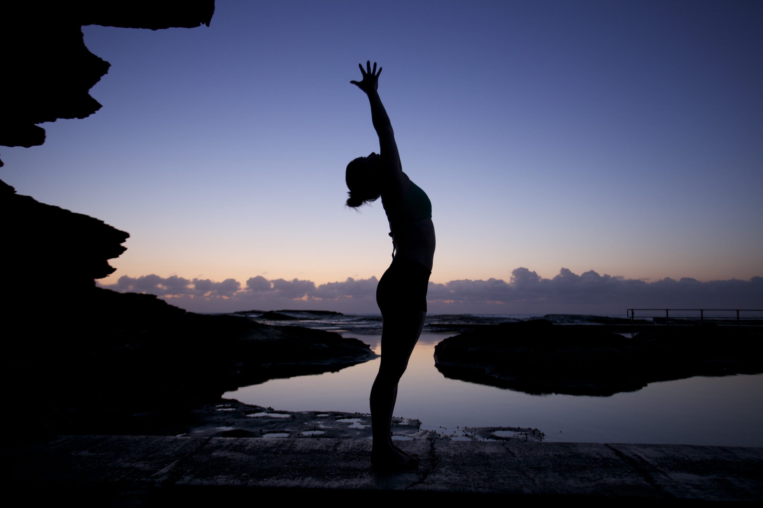 Woman doing yoga at dusk at the beach