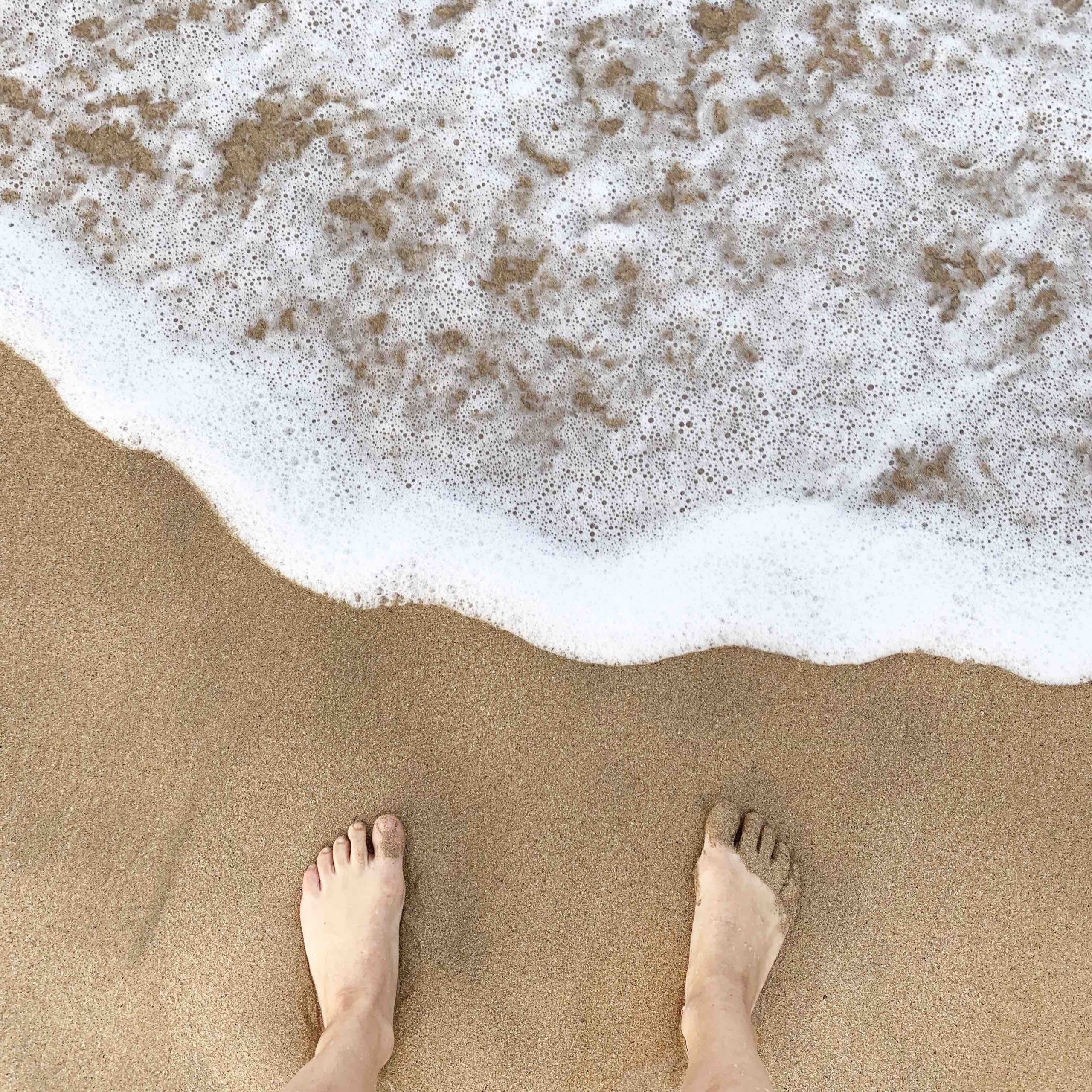 Feet standing in the sand near the waves