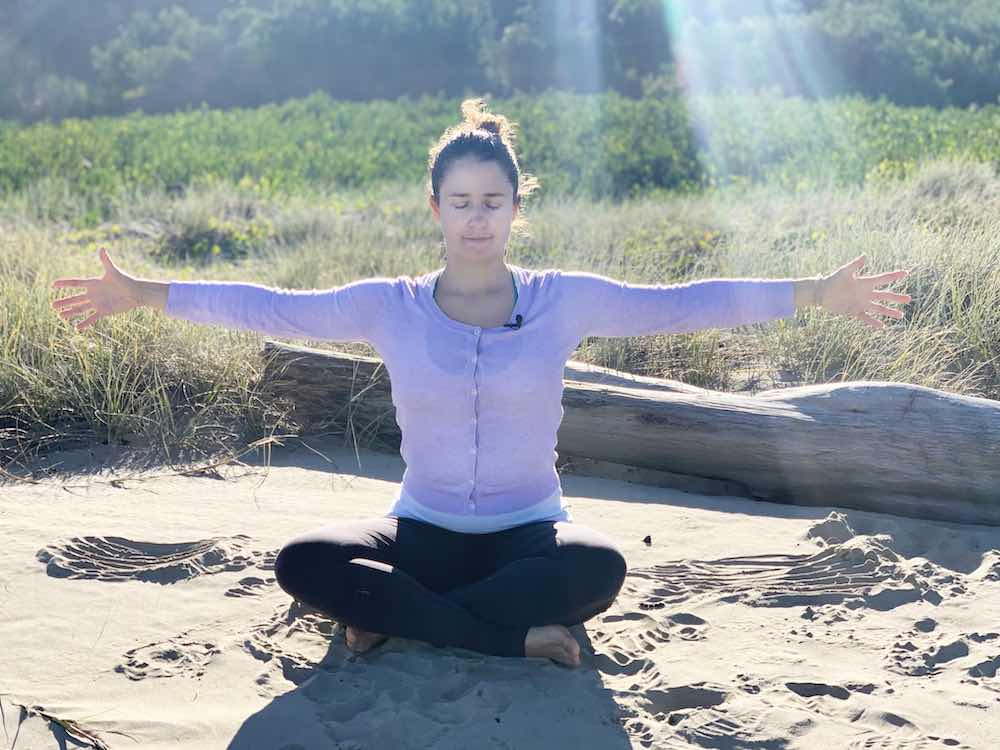 Woman sitting at a beach doing some mindful movement and breath-work meditation