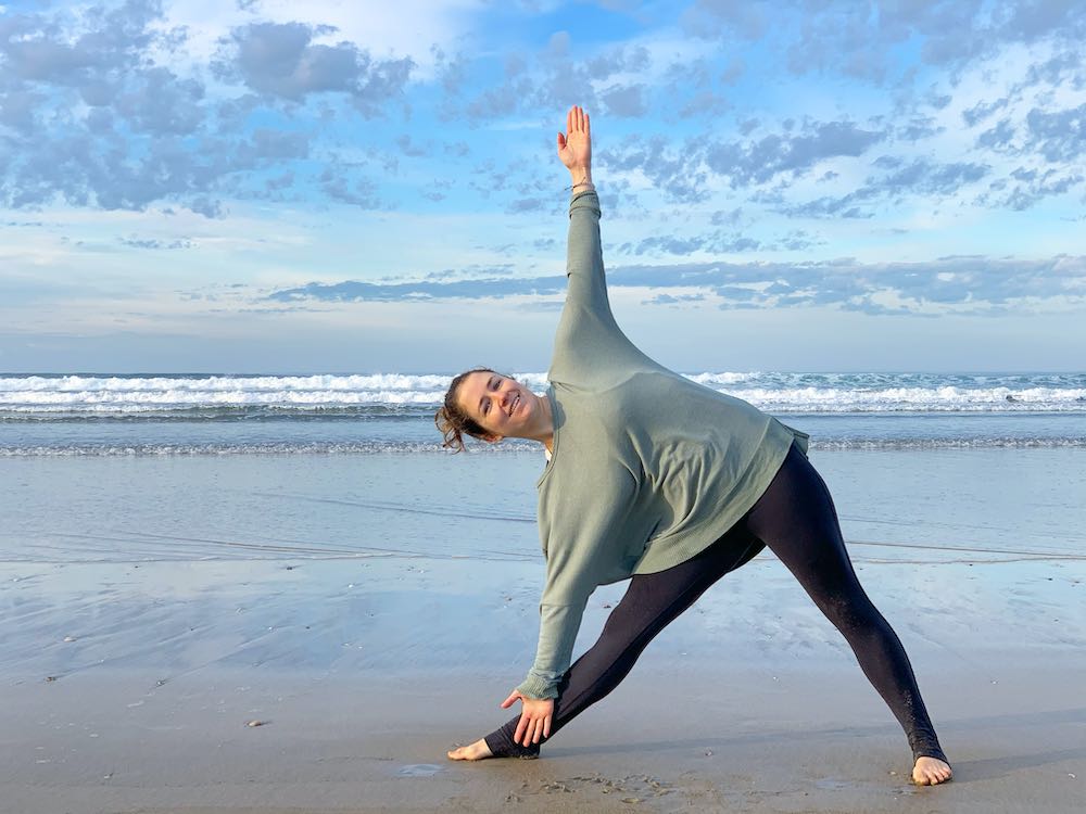 Woman doing Trikonasana (Triangle Yoga Pose) at the beach